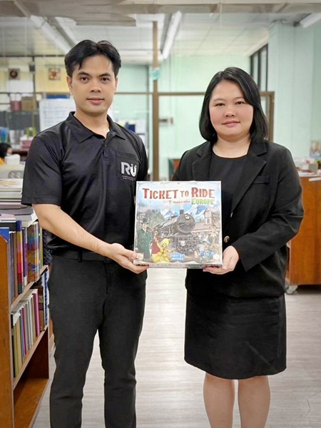 ภาพอาจารย์พิมพ์ชนก โพธิปัสสา (ขวา) รองผู้อำนวยการฝ่ายวิชาการและวิจัย สำนักหอสมุดกลาง มอบบอร์ดเกม โดยมีนายอัศม์ธรีนณ์ ศุภกิจวรสิทธิ์ (ซ้าย) หัวหน้าหน่วยพัฒนาทรัพยากรสารสนเทศ เป็นผู้รับมอบ