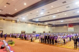 ภาพผู้ช่วยศาสตราจารย์วุฒิศักดิ์ ลาภเจริญทรัพย์ กล่าวคำถวายราชสดุดีเฉลิมพระเกียรติ และผู้เข้าร่วมพิธีร้องเพลงสรรเสริญพระบารมี